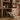 Wooden kitchen cabinet with open drawer displaying wine bottles and snacks, tiled wall in the background.