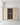 Wooden wine cabinet with wine bottles inside, in a bright room with large windows.