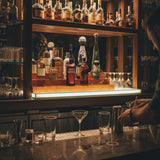 Bar counter with bottles and glasses, illuminated by a warm light.