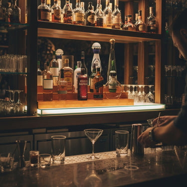 Bar counter with bottles and glasses, illuminated by a warm light.