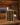 Wine rack with bottles, a candle, and a glass of wine on a wooden table in a cozy room with a fireplace.