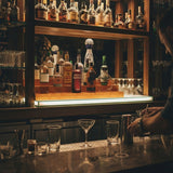 Bar setup with various bottles and glasses, illuminated by warm lighting.
