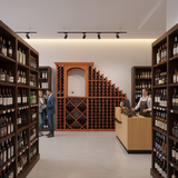 Wine store interior with shelves stocked with bottles, a counter, and people interacting.