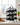 Black metal wine rack holding bottles on a kitchen counter with a cityscape view.