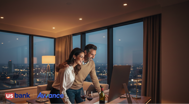 Couple in a modern living room with a cityscape view, using a computer. US Bank Advance logo visible.