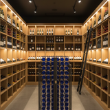 Wine cellar with wooden shelves filled with bottles, a ladder, and a rack of blue bottles.