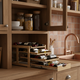 Wooden kitchen cabinet with open drawer displaying wine bottles and snacks, tiled wall in the background.