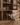 Wooden kitchen cabinet with open drawer displaying wine bottles and snacks, tiled wall in the background.