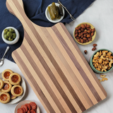 Wooden serving board with striped pattern on a white surface with snacks.