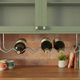 Wine bottles on a rack above a wooden counter with books and a plant.