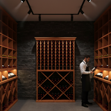 Man in a wine cellar examining bottles with wooden shelves and lighting fixtures.