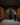 Person in a wine cellar inspecting bottles among wooden shelves.