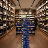 Wine cellar with shelves stocked with bottles and a person inspecting them.
