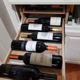 Wine bottles arranged in a wooden drawer within a kitchen cabinet.